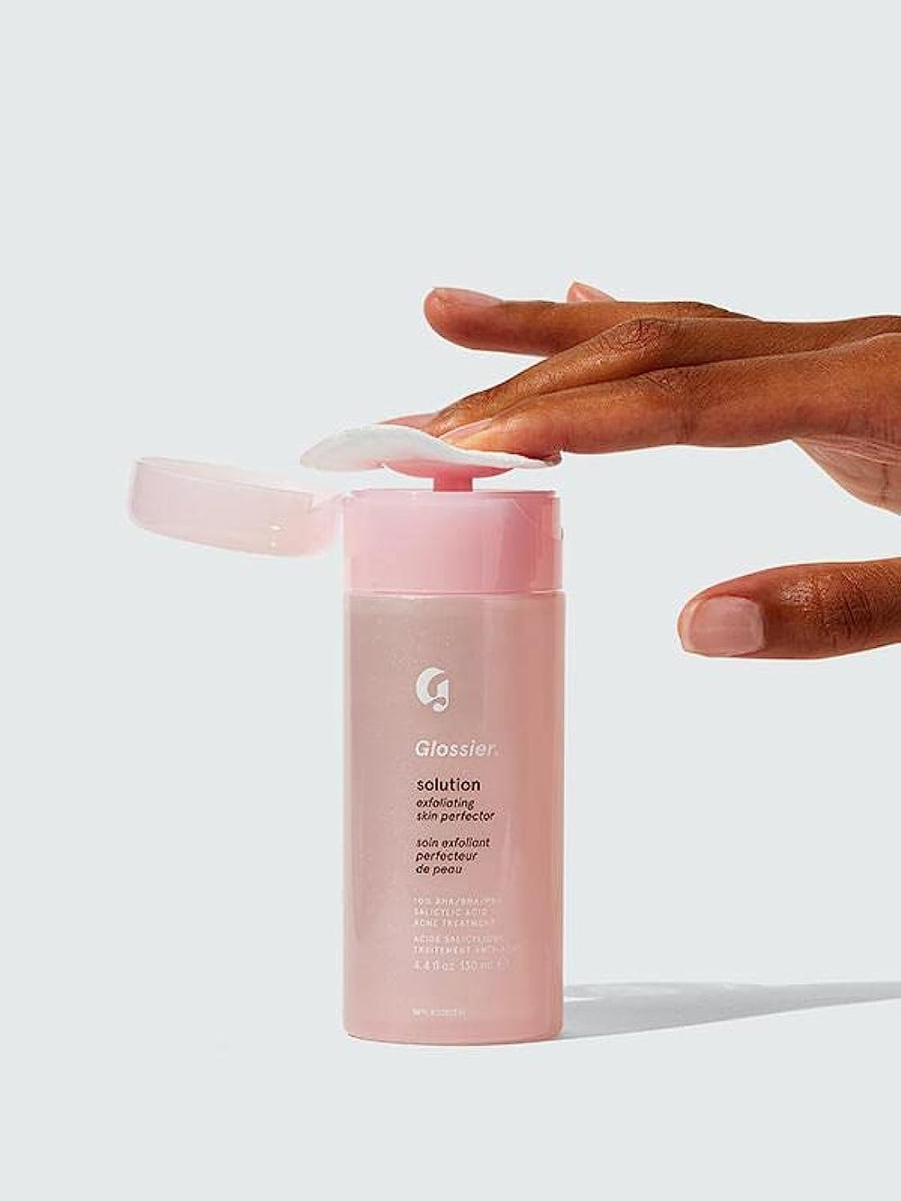 Glossier Solution bottle on shelf, exfoliant for smoother skin texture.