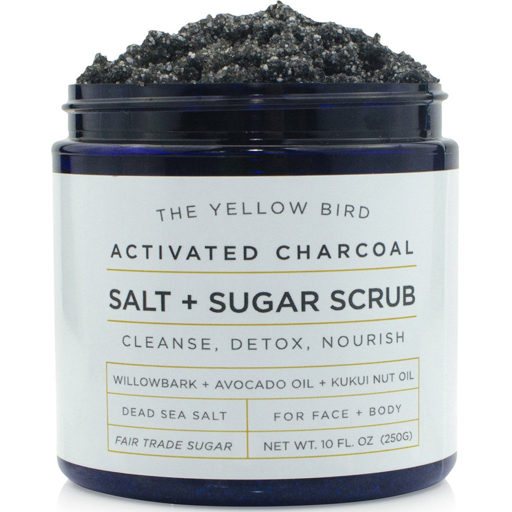 The Yellow Bird charcoal scrub jar closeup highlights rich exfoliant texture for smooth skin.