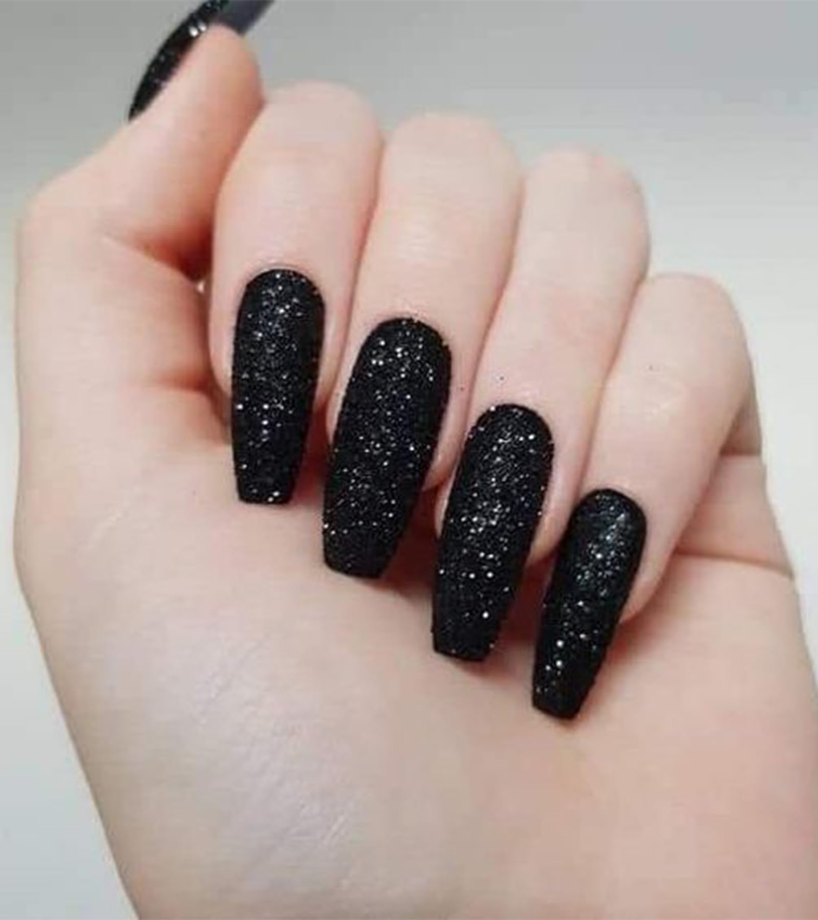 Aegenacess close-up of hands wearing long black glitter coffin nails.