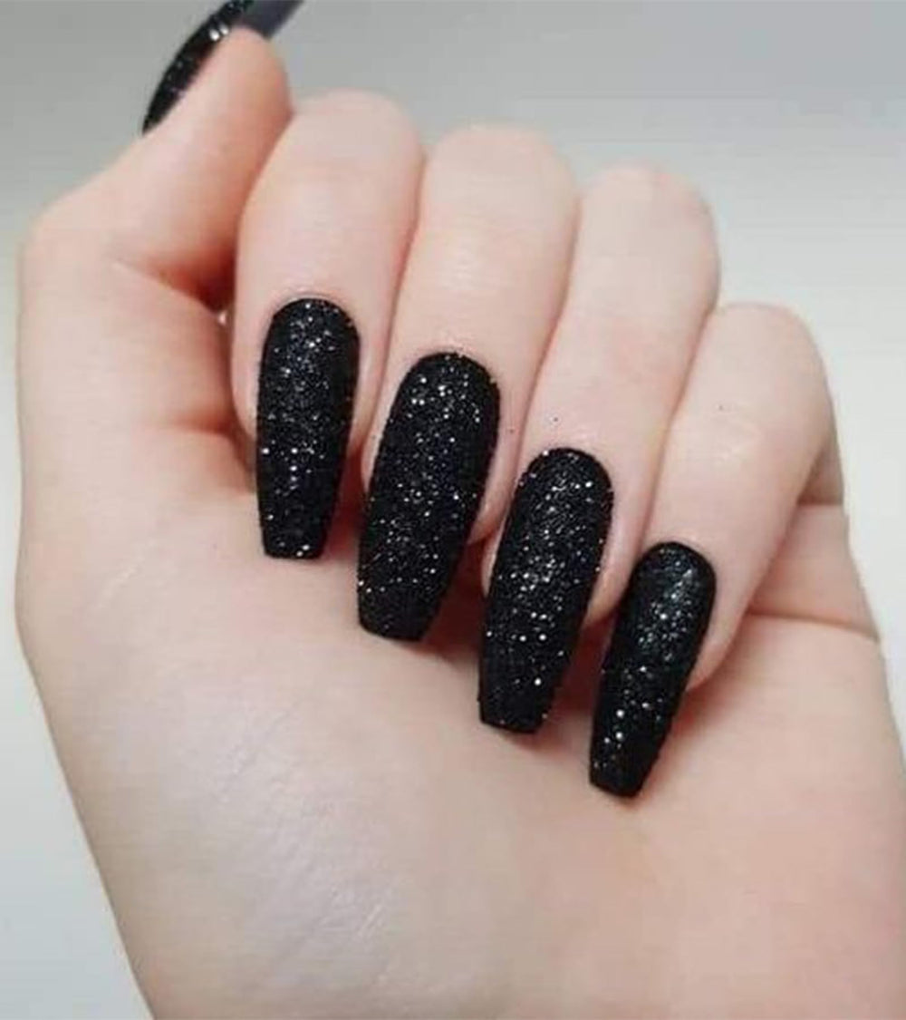 Aegenacess close-up of hands wearing long black glitter coffin nails.