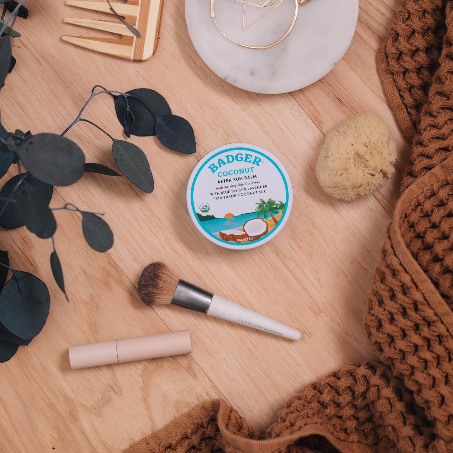 Travel-friendly Badger Coconut AfterSun Balm tin in a beach bag