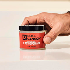 Hands applying Duke Cannon pomade demonstrates even distribution