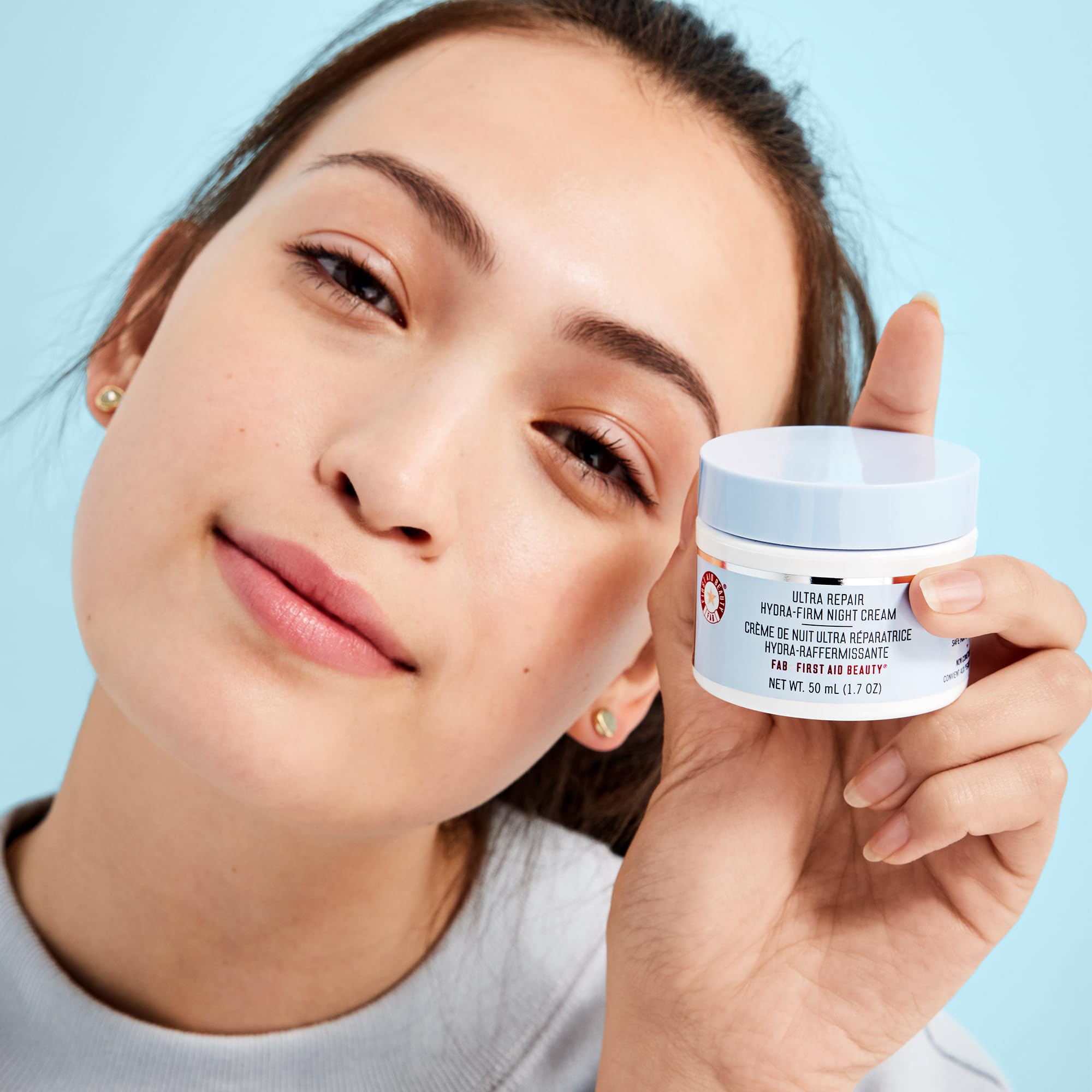 First Aid Beauty skin-care bottle on skin communicates hydration and comfort.