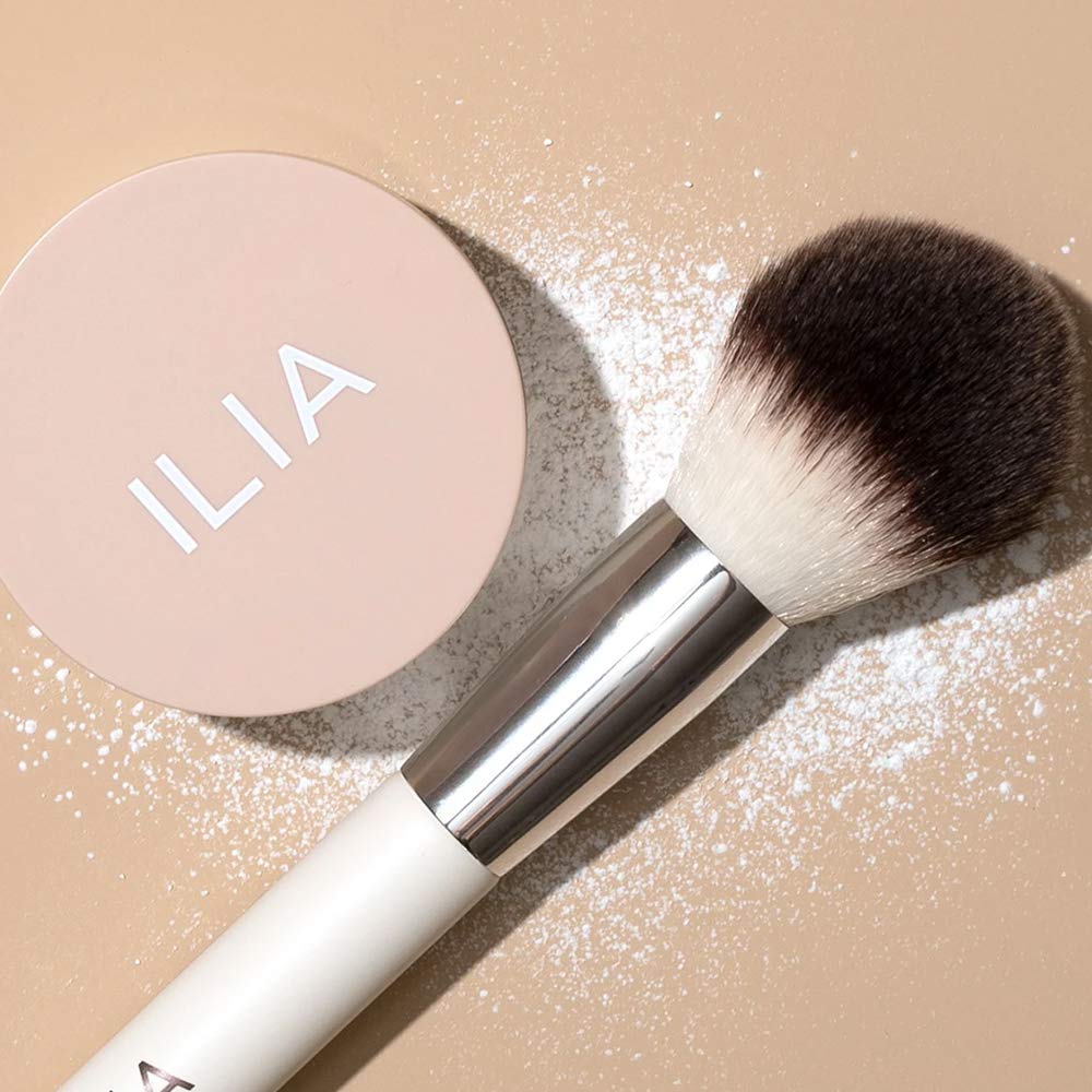 Close-up of brush applying ILIA Soft Focus Setting Powder for even coverage.