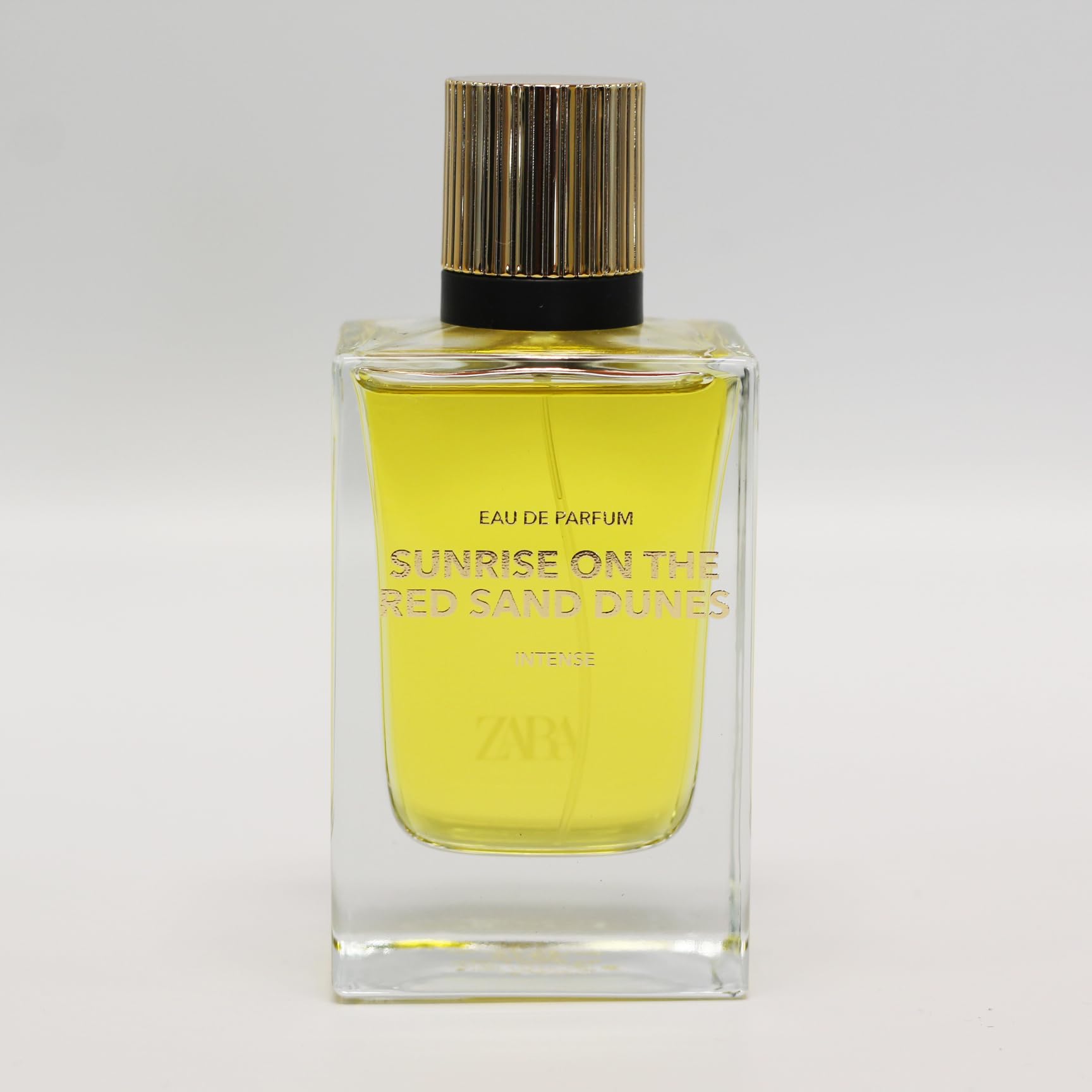 Zara Sunrise bottle cap against red dunes, suggesting refined luxury and portable scent